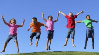 Dzieci skaczą na zielonej łące, bezchmurne niebo
