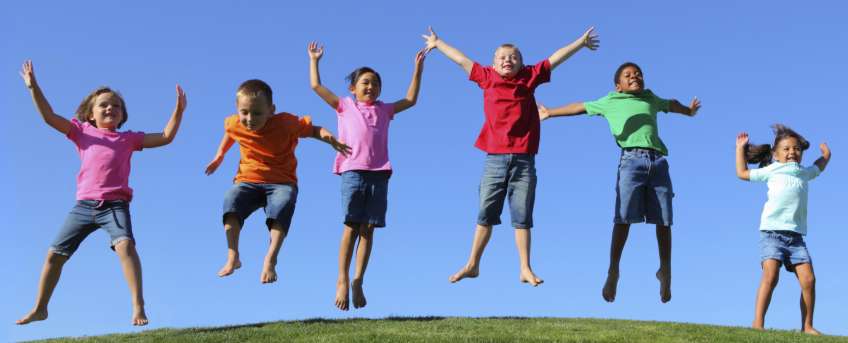 Dzieci skaczą na zielonej łące, bezchmurne niebo